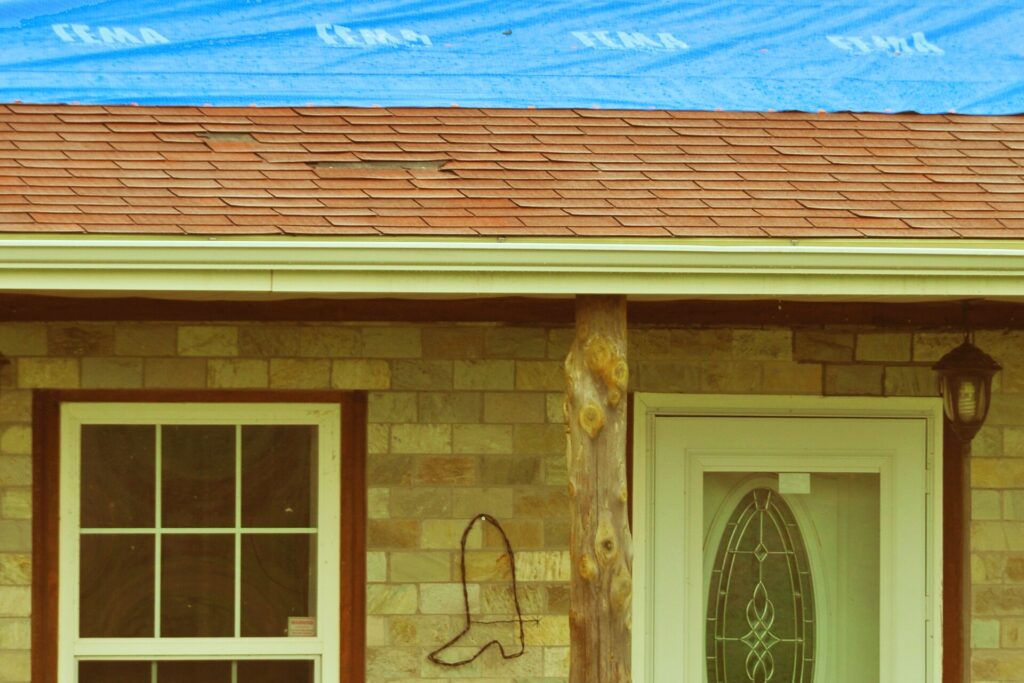 Storm-damaged house roof covered with a tarp, illustrating actual cash value vs replacement cost claims